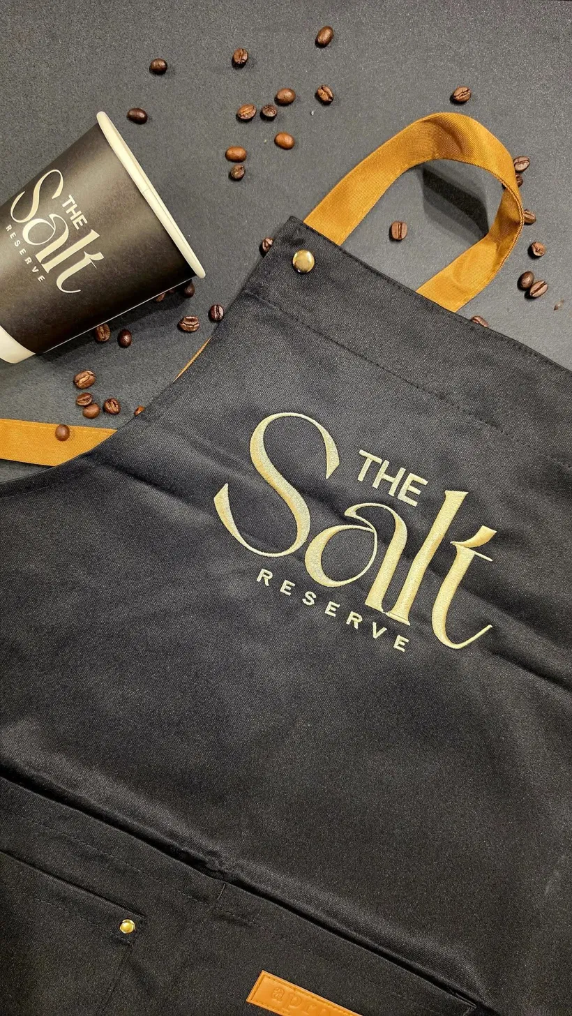 Black apron, branded cup, and roasted beans from The Salt Reserve